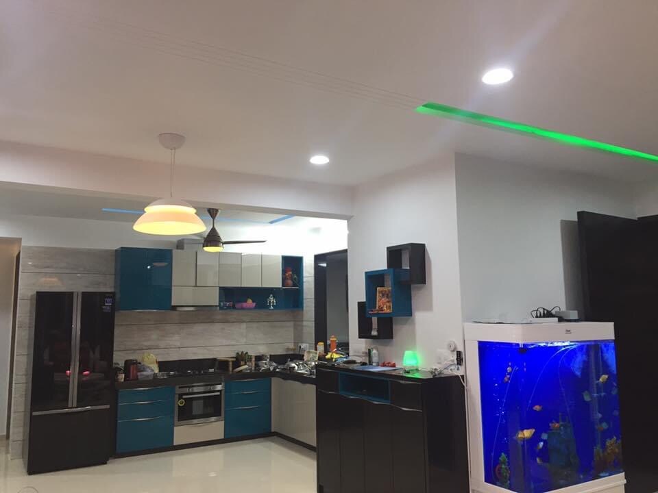 A modern kitchen features a combination of blue and black cabinetry, complemented by stainless steel appliances. An aquarium filled with colorful fish serves as a focal point. Bright overhead lights illuminate the space, highlighting the organized layout and functional design.