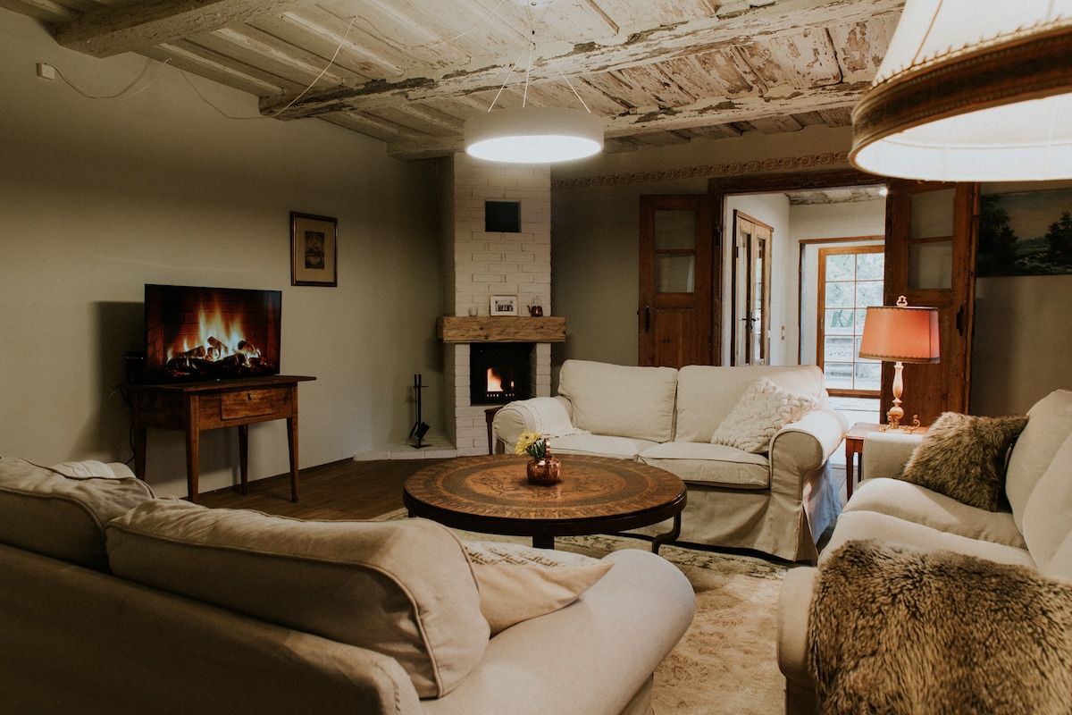 A comfortable living area features a circular coffee table at the center, surrounded by soft sofas. A flat-screen television is mounted on the wall, with a fireplace adding warmth to the space. Nearby, glass doors provide access to the outdoor area.