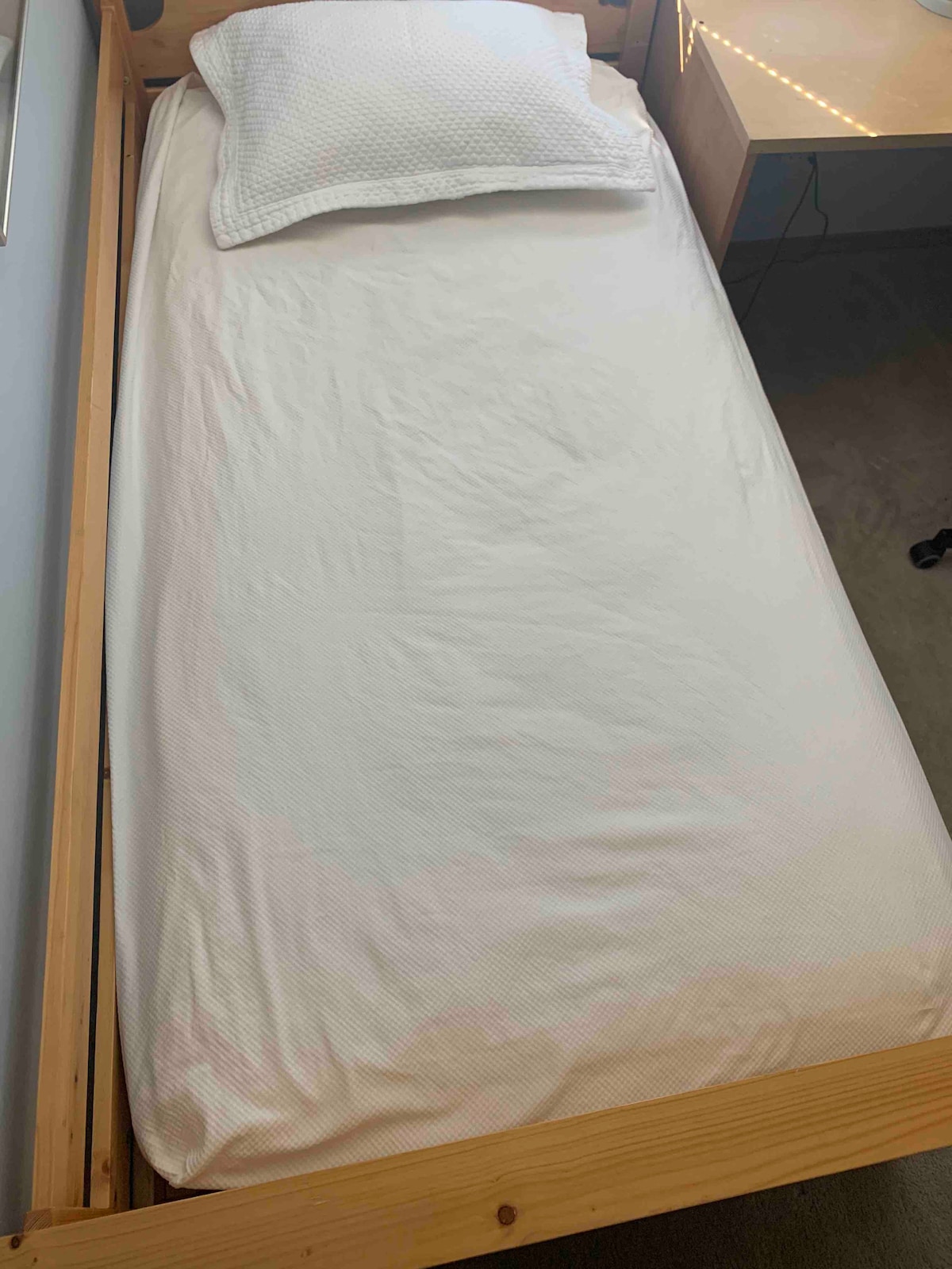 A neatly made bed features a light-colored fitted sheet and a single pillow resting at the head. The wooden frame provides a warm touch to the room's decor.