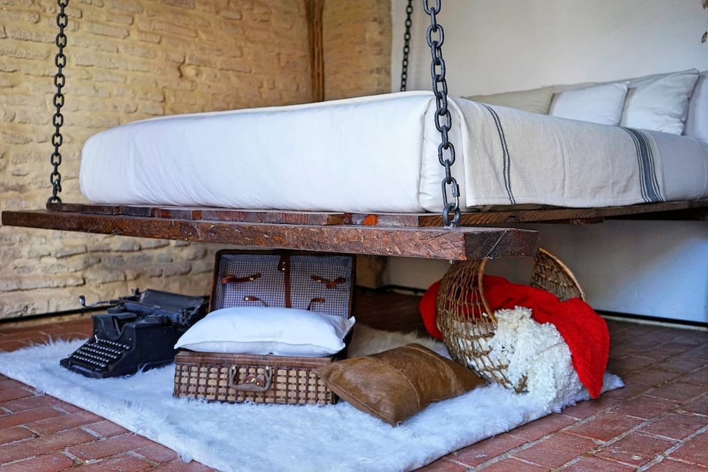 The real hanging bed anchored to the wood beam roof and a collection of goodies underneath the bed.