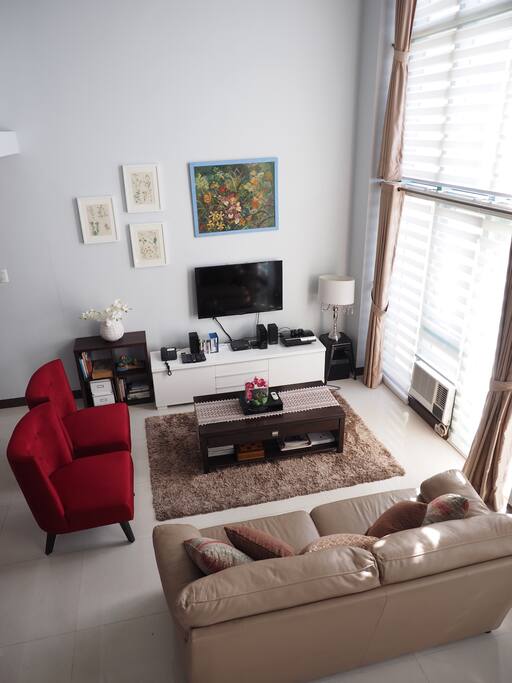 Open Plan Living Room with high ceilings, comfortable couch and chairs and plenty of natural light with the blinds and curtains to block the heat and sun