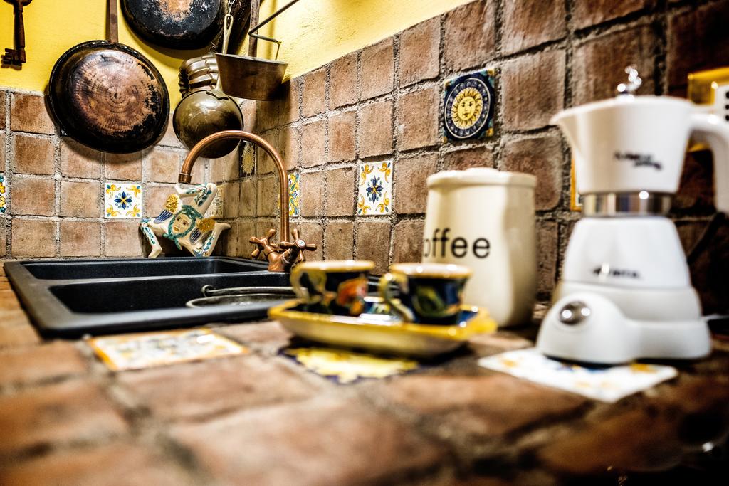 A charming kitchen space features rustic tiled surfaces in warm tones, complemented by colorful ceramic accents. A modern coffee maker sits near traditional espresso cups on a plate, while a unique faucet adds character to the stone sink area.