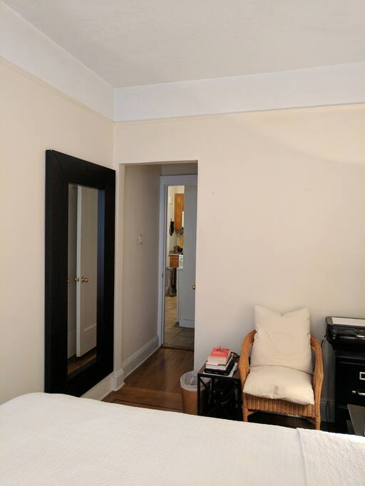 Bedroom: long mirror hung off the ground on the wall; chair and side table.