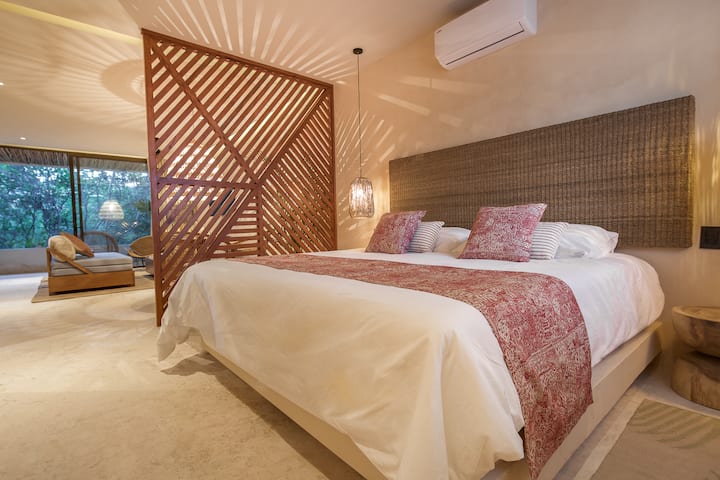 Cama king size con celosía de diseño que separa la zona del salón con sofá cama king size y vista de la terraza privada.