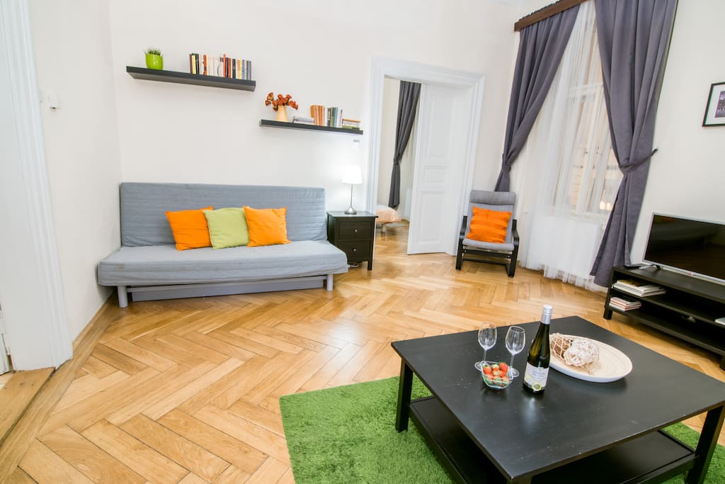 A spacious living room with an original parquet floor. Equipped with two folding sofas, two armchairs and television
