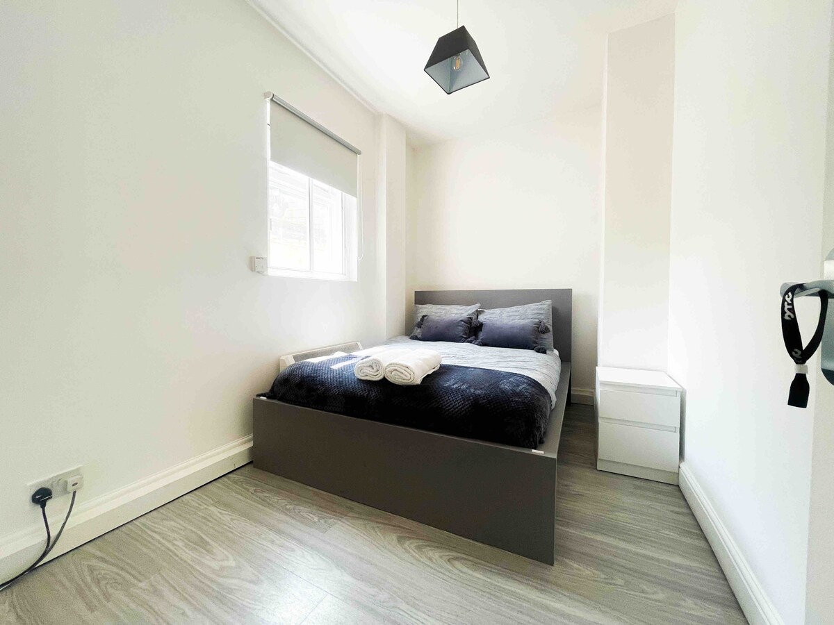 Уютна спалня с двойно легло до голям стъклен прозорец, с двуслойно малко нощно шкафче за удобно съхранение и лесен достъп до най-важното.