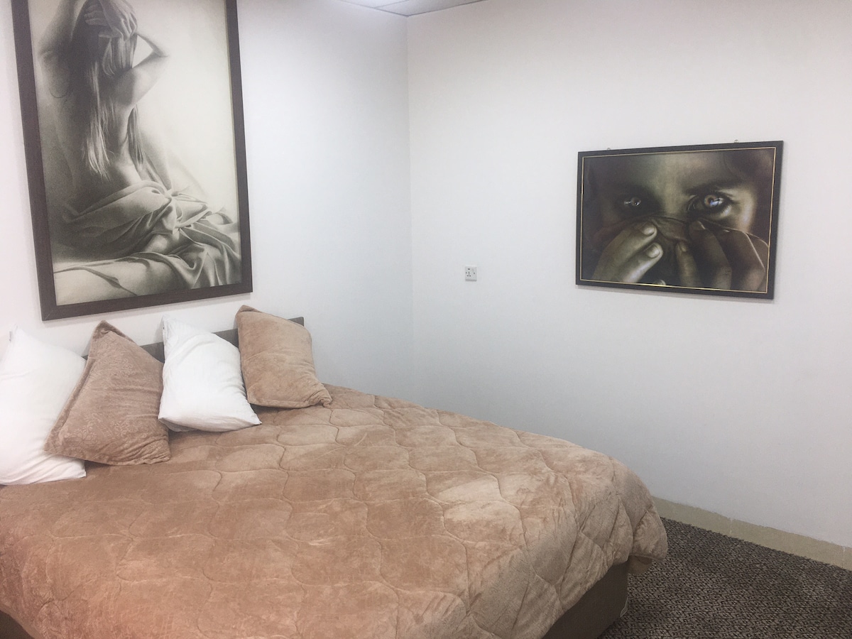 A comfortable sleeping area is furnished with a spacious bed covered in a soft brown quilt. Decorative pillows add a cozy touch. Art displays featuring black-and-white photography adorn the walls, offering a modern aesthetic to the room.