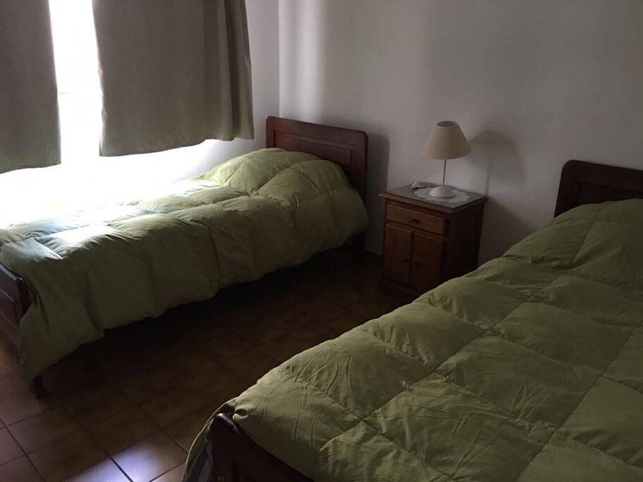 Dormitorio con vista al pulmón del edificio, armario, dos camas, mesa de luz, velador, calefacción, plumones, mantas y sabanas.