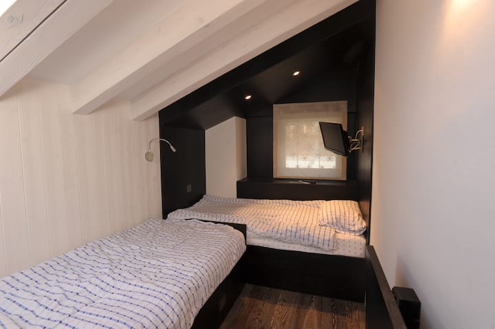 Chumba cha kulala pacha na ukuta uliowekwa kwenye televisheni na kukunja dawati chini, vyumba vya kuning 'inia, kabati, chini ya droo za kitanda, na dirisha la glazed mara tatu