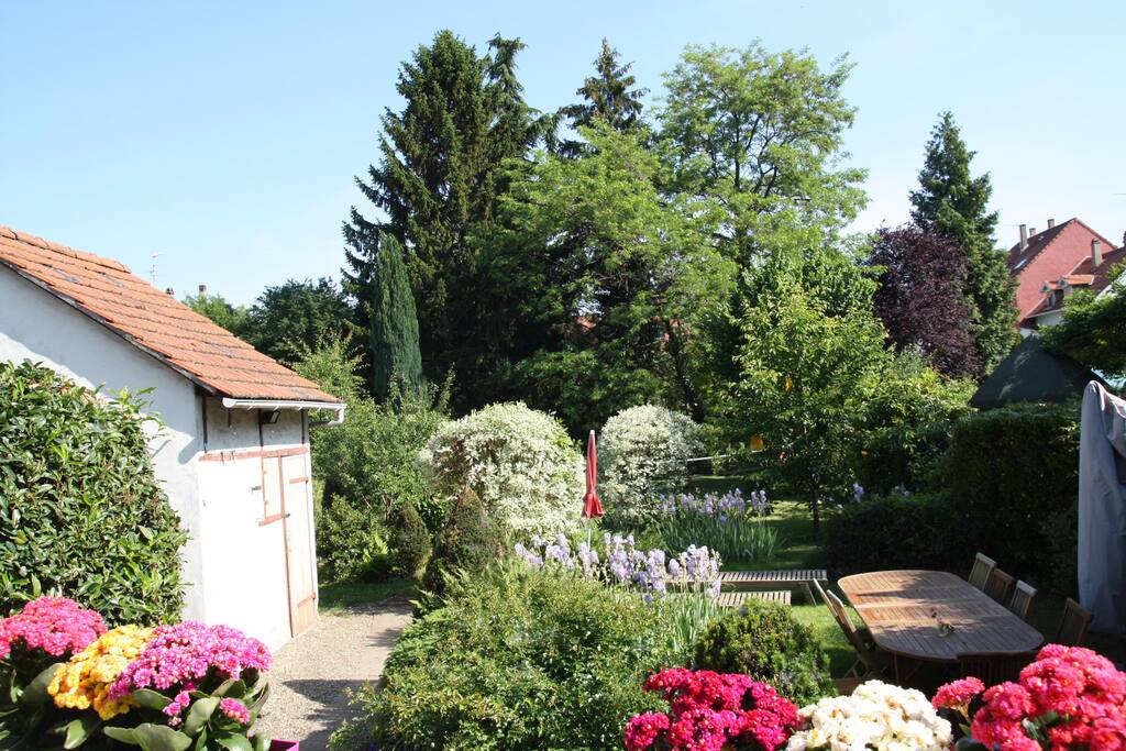 Le jardin fleuri, harmonieux et accueillant avec sa grande table en bois et son parasol ...