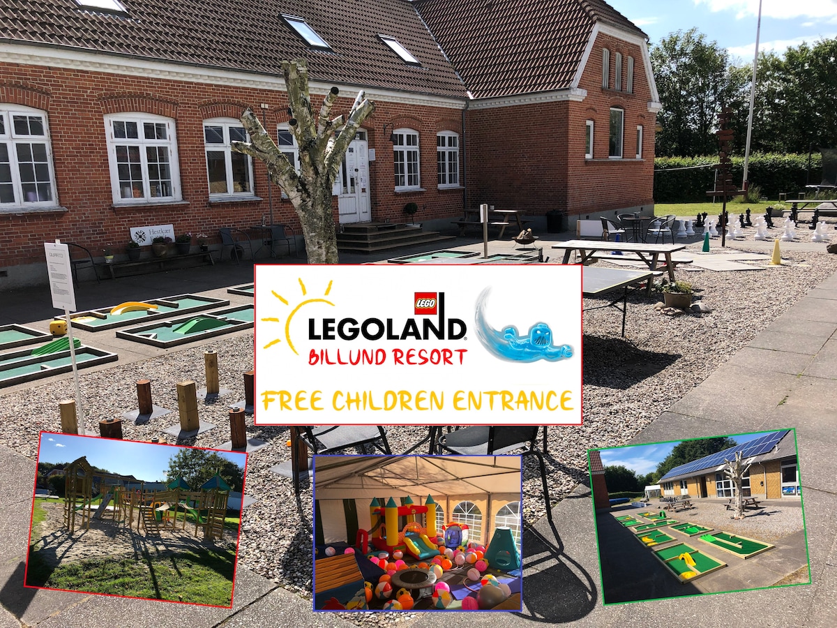 An outdoor area features a colorful play structure surrounded by sand and gravel. Miniature golf is also visible, with several playful greens. A large sign promotes free children's entrance to Legoland Billund Resort, signifying family-friendly activities are offered.