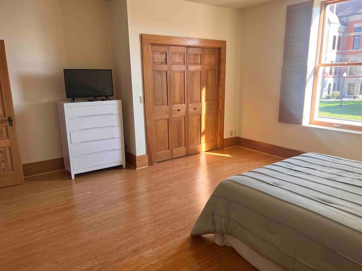 El dormitorio 1 contiene una cama tamaño queen, vestidor, televisión inteligente, silla y armario.  ¡Cada dormitorio tiene una vista de la plaza del juzgado!  