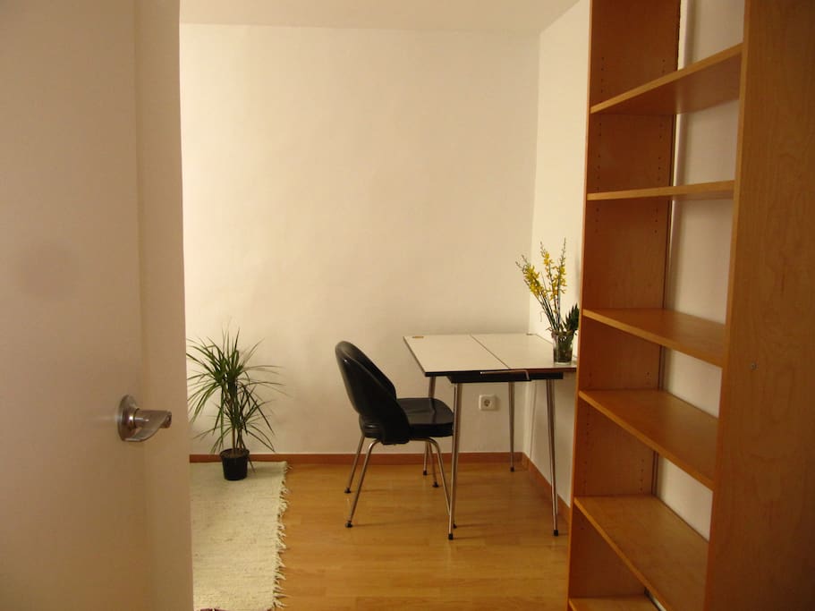 Private room with desk, mirror, shelving and fan.