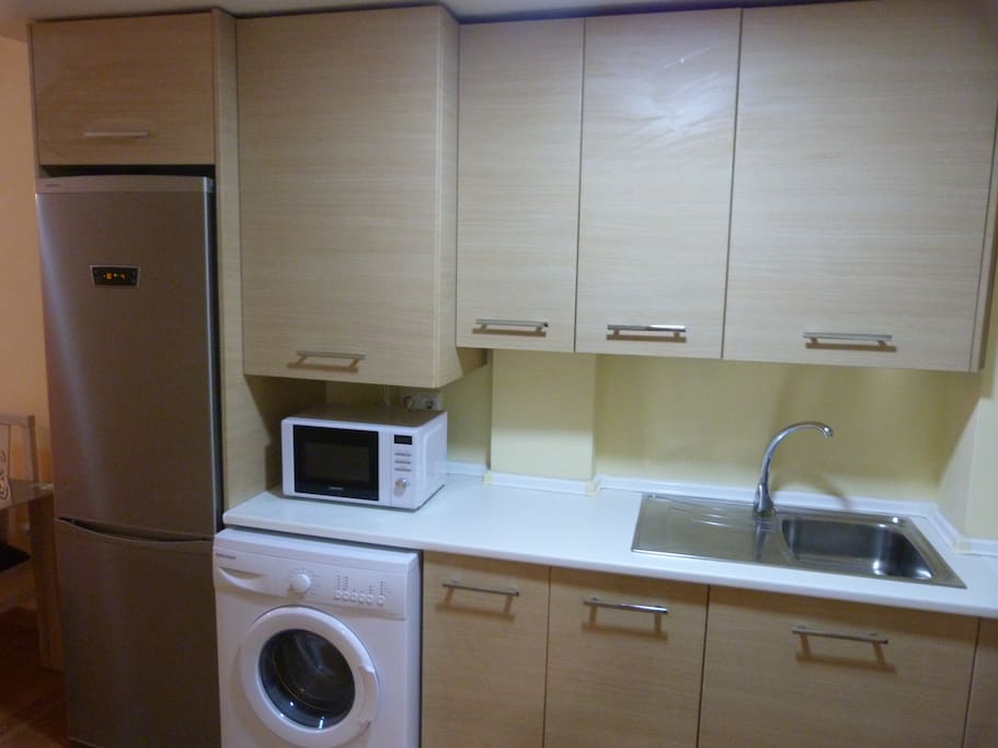 Cocina equipada con nevera-congelador combi alta gama, lavadora, microondas, horno, placa vitrocerámica, extractor de humos, tostador de pan, exprimidor de zumos, cafetera, batidora, menaje completo para cocinar, cubertería, y vajilla completa.