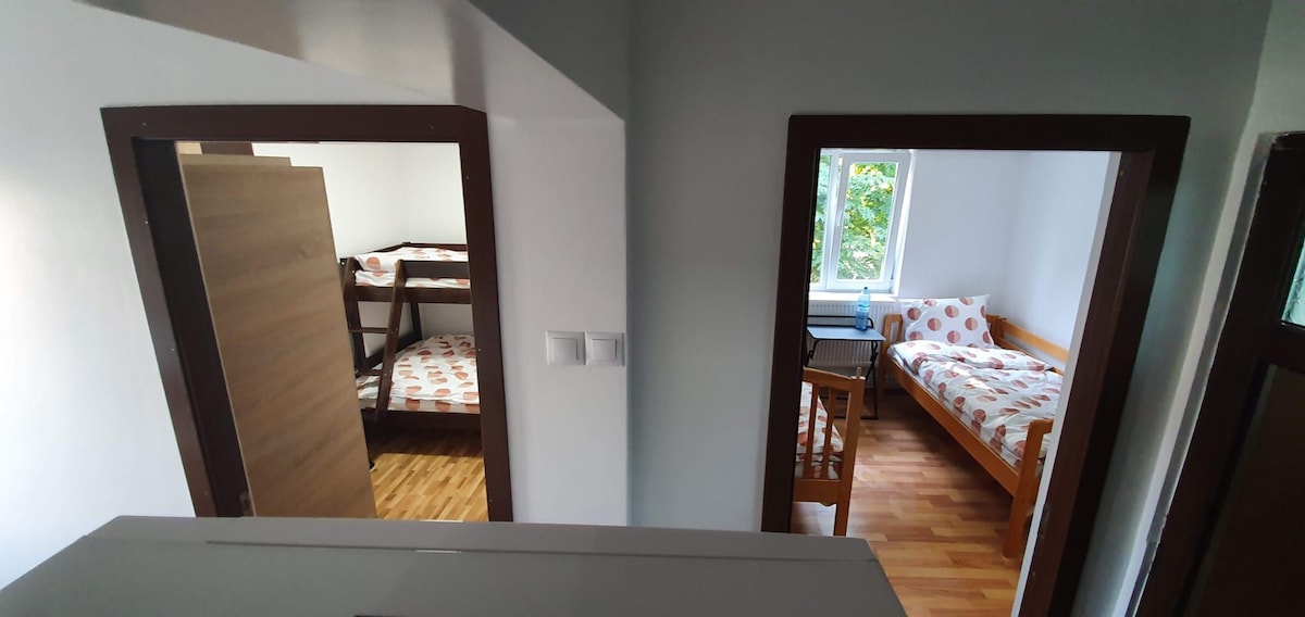 A view from above displays two separate sleeping areas. One room features a bunk bed with a dark wood finish, while the other offers a single bed adorned with a polka dot patterned bedding. Natural light enters through a nearby window, illuminating the wooden floor.