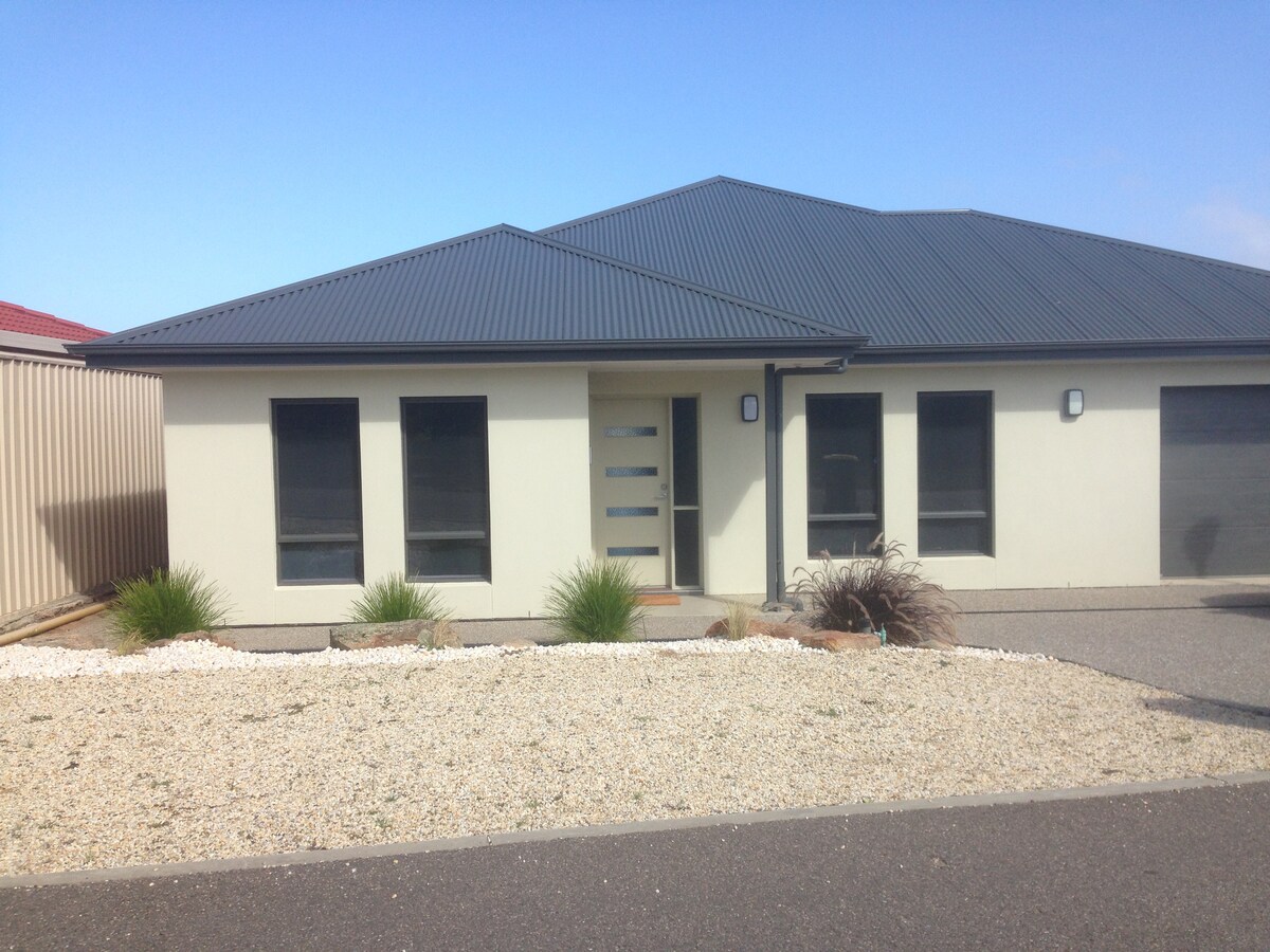 The modern exterior of the property is showcased with a well-maintained landscape featuring gravel and bush-like plants. The front entrance is highlighted by a sleek door and large windows, allowing natural light to illuminate the interior.