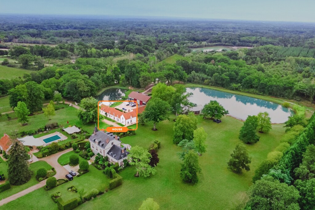 An aerial view of a sprawling property showcases a charming two-story house nestled among lush greenery and a tranquil pond. The outdoor area features a pool and pathways bordered by trees, creating a serene and spacious landscape.