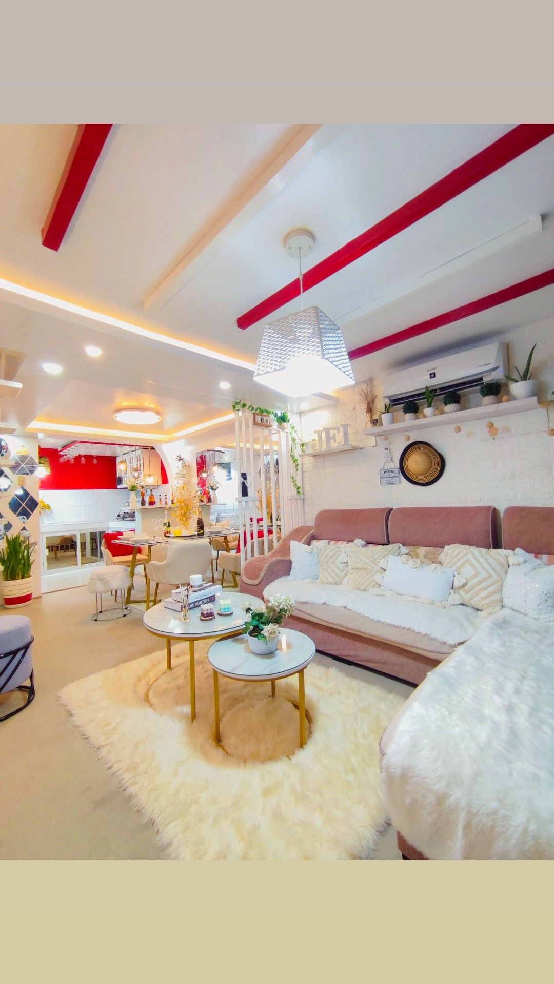 A cozy living area features a plush sofa adorned with decorative cushions. A soft, light rug covers the floor beneath two round coffee tables, which are topped with plants and decorative items. Warm lighting highlights the inviting atmosphere.