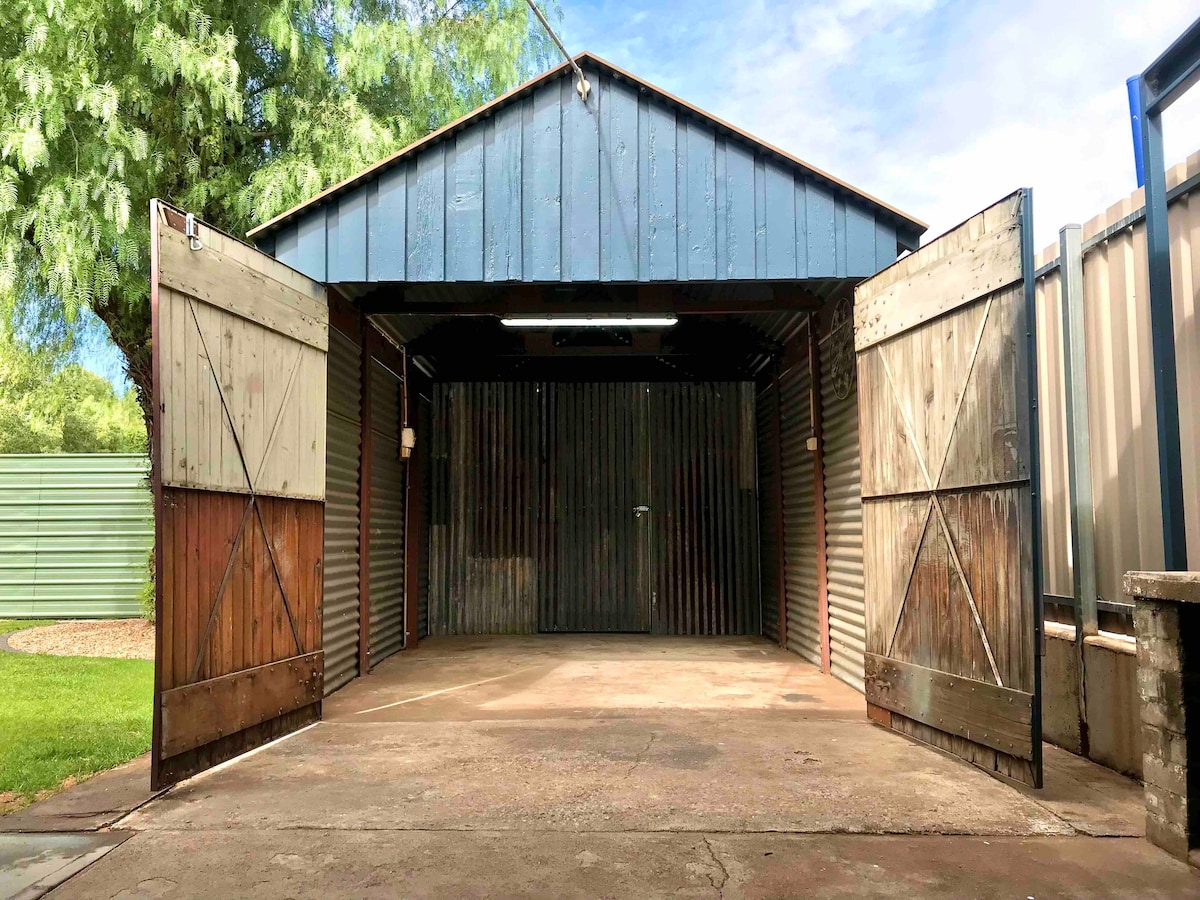 A powered shed is presented with double wooden doors wide open, revealing a spacious interior with a concrete floor. The walls are constructed from corrugated metal, and overhead lighting is clearly visible, providing ample illumination for various uses.