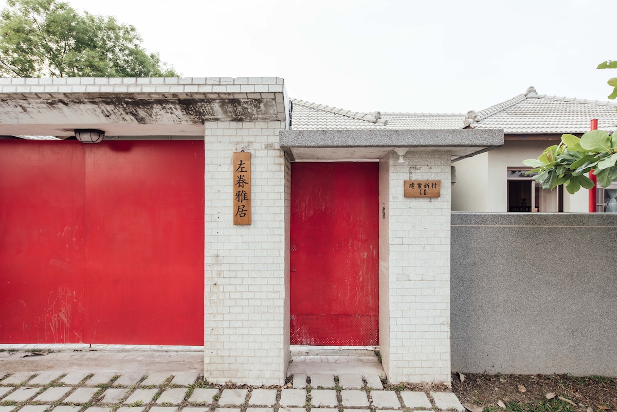 A distinctive entrance is highlighted by vibrant red doors, flanked by white brick walls. The surroundings feature a neatly paved stone pathway leading to the entrance, contributing to a welcoming and accessible entryway for guests.