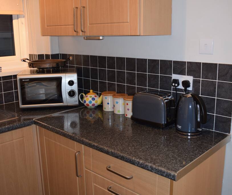 Kitchen with gas cooker and oven, fridge, microwave, kettle, toaster, cutlery and utensils.