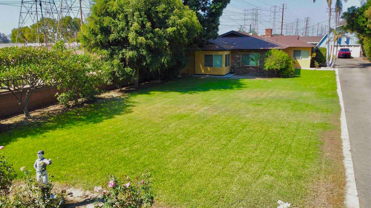 A spacious front yard features well-maintained green grass, bordered by trees and shrubs. A decorative statue is visible along with a pathway leading to the home. The property is set back from the street, providing an unobstructed view of the inviting outdoor space.