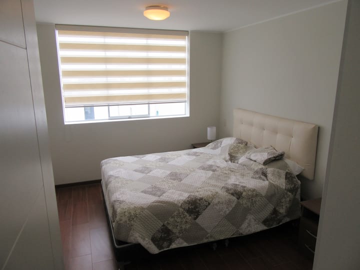 Spálňa s priestrannou manželskou posteľou, kde si môžete pokojne oddýchnuť po náročnom dni, nočné stolíky, šatník a 32-palcovú inteligentnú televíziu na stene.