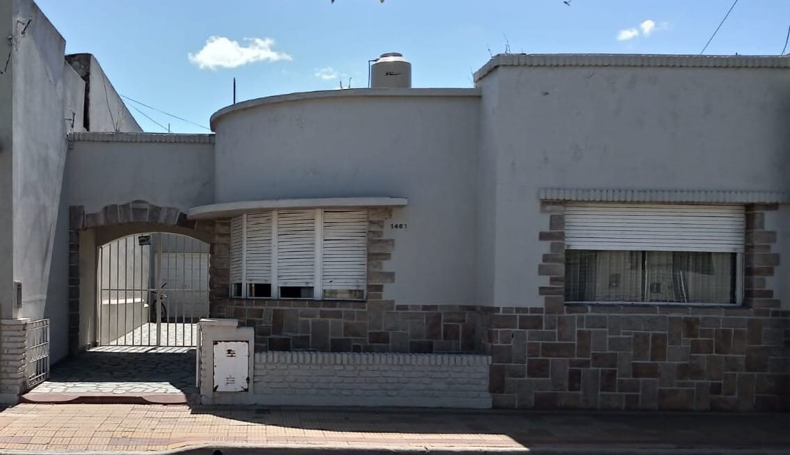 The exterior of the property features a modern design with a smooth, light-colored facade and stone accents. A rounded window is noticeable on the side, and a gated entrance leads to an outdoor area. Surrounding space is open, contributing to a welcoming atmosphere.