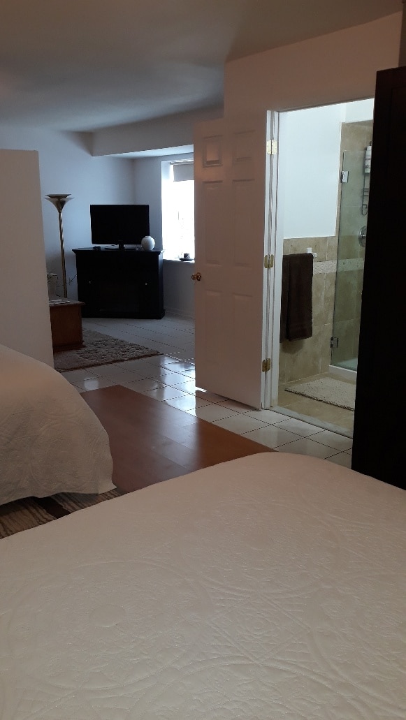 A spacious interior is visible, featuring two queen beds and a partial view of a bathroom with a walk-in shower. A flat-screen television is positioned in the living area, illuminated by natural light from the nearby window.