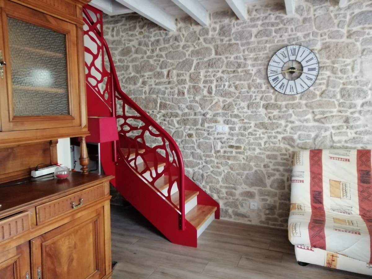A wooden cabinet is positioned beside a comfortable seating area adorned with a patterned throw. A distinctive red staircase with decorative railing leads to the upper level. A clock is mounted on the stone wall, adding functional decor to the inviting living space.