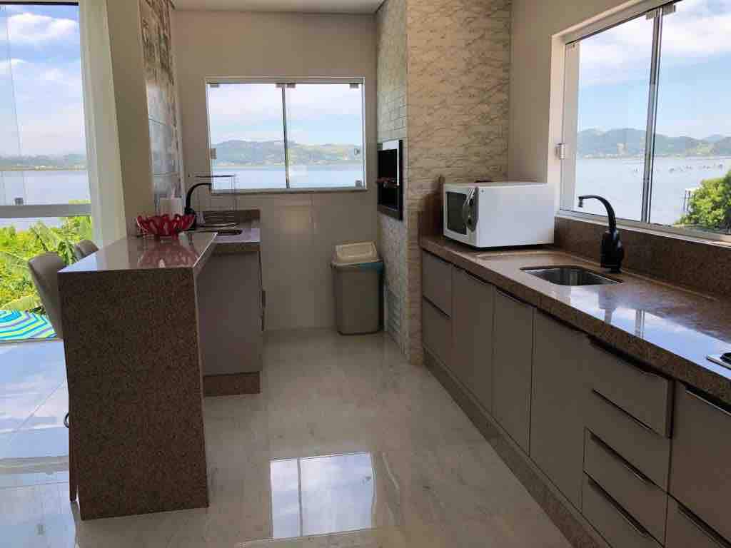 A modern kitchen features sleek cabinets and a spacious countertop, with a view of the surrounding landscape through large windows. Natural light fills the area, highlighting the neutral color scheme. Essential appliances, including a microwave, are integrated into the design.