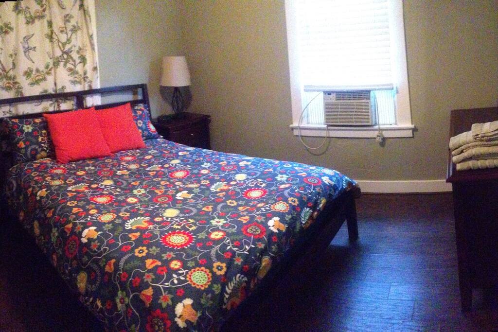 Relaxing room with queen bed, nightstand, desk, dresser, mirror, closet, alarm clock, reading lamp, wood laminate flooring, and remote control overhead lamp and adjustable fan. Heater and ac unit for personal preference.