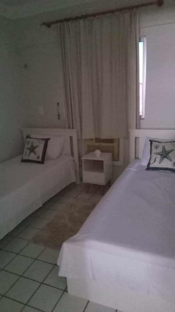 Habitación con dos camas individuales,  aire acondicionado,  bidé, armario en los estantes, espejo, ventilador y lugar para poner la hamaca.  Con almohadas, ropa de cama, toallas de baño, toallas de cara y suelo. Con mosquiteras en la ventana