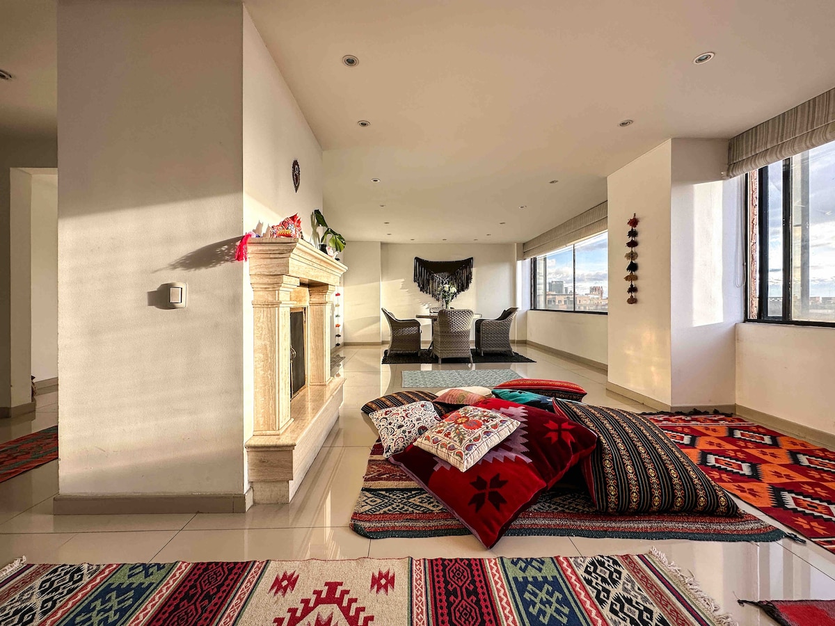Vista desde la habitación principal a la hermosa y cálida sala de chimenea y comedor con tapetes y cojines traídos de diferentes partes del mundo.  