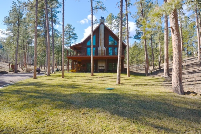 A modern rustic cabin stands among towering pine trees, showcasing its distinctive gabled roof and large glass windows. A well-maintained lawn encircles the home, providing a serene outdoor space that connects with the natural surroundings.