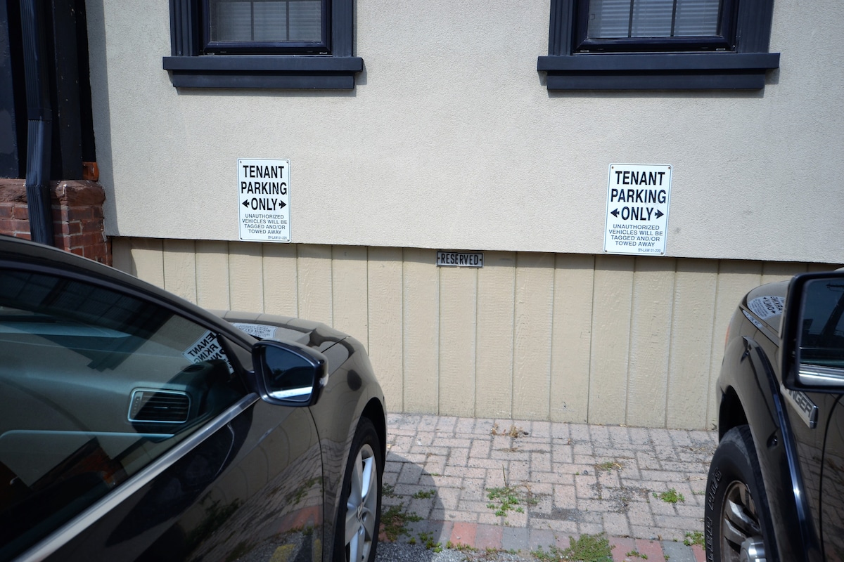 A designated parking area is depicted, with clear 'Tenant Parking Only' signs displayed on the wall. Two vehicles occupy the space, and the ground is paved with bricks, providing a tidy and organized appearance. The wall above displays a reserved number marker.
