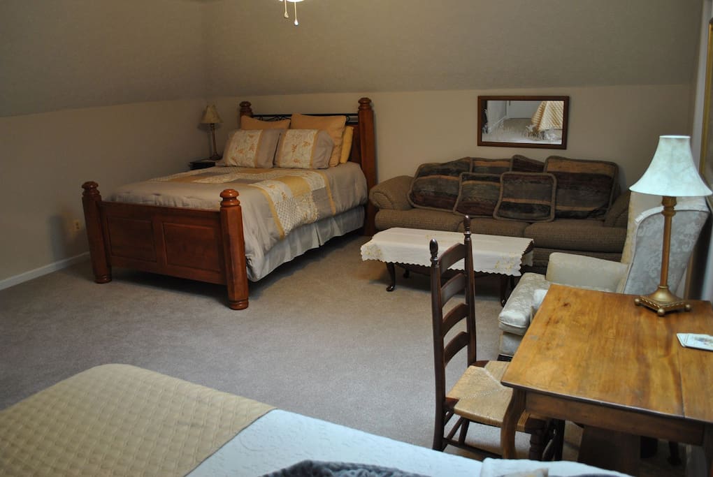 View of room from the full bed showing full sofa and queen bed with desk in the foreground.