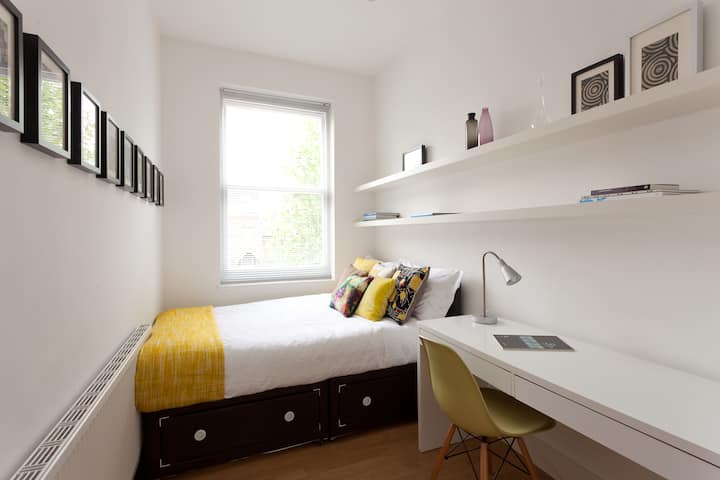 غرفة نوم بيضاء مع لمسات من اللون الأصفر ومكتب لتدوين معالم لندن 