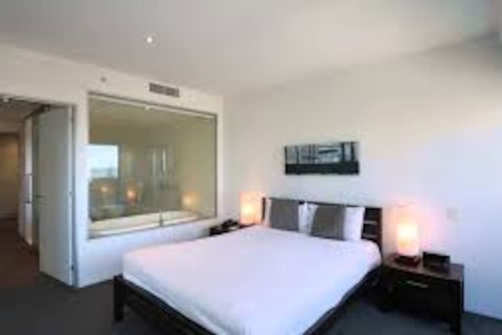 Bathroom has spa and window into bedroom which does hava a blind
