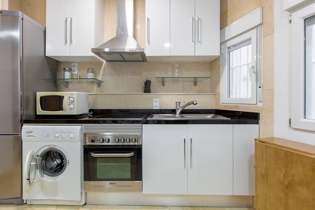 Cocina americana nueva completamente equipada con encimera de granito negro, frontal de mármol beige, muebles nuevos