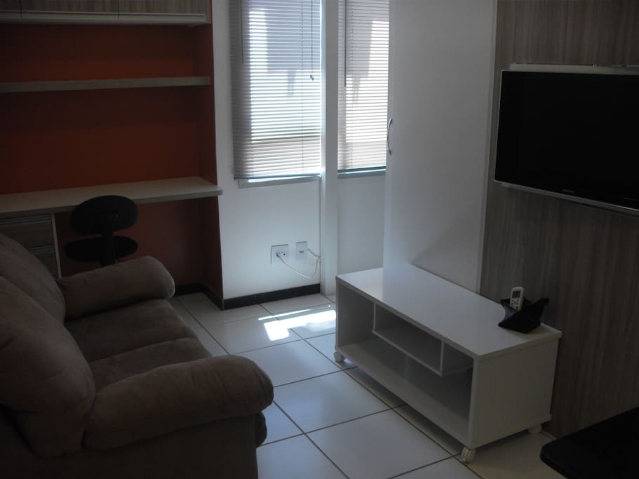 Sala mobiliada com sofá-cama, tv giratória, escrivaninha e armários