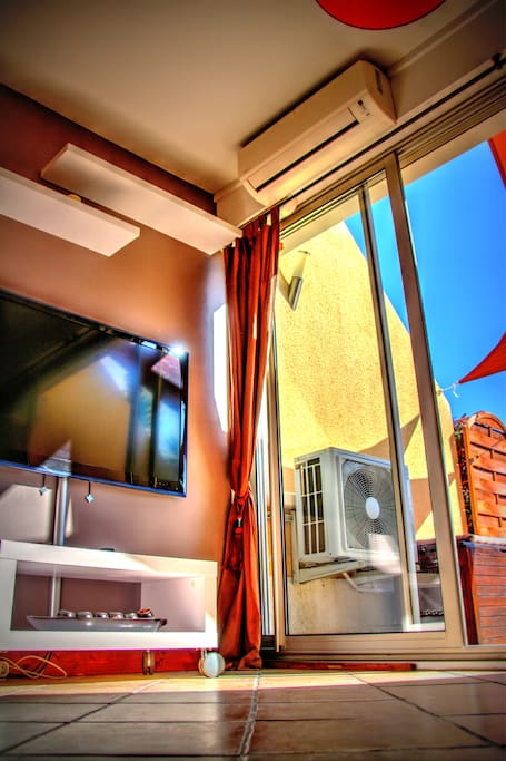 salon équipé d'un BZ avec vue sur une grande terrasse ensoleillé, barbecue dans le fond de la terrasse pour des repas au soleil, Tv led de 119cm, climatisation réversible daikin.