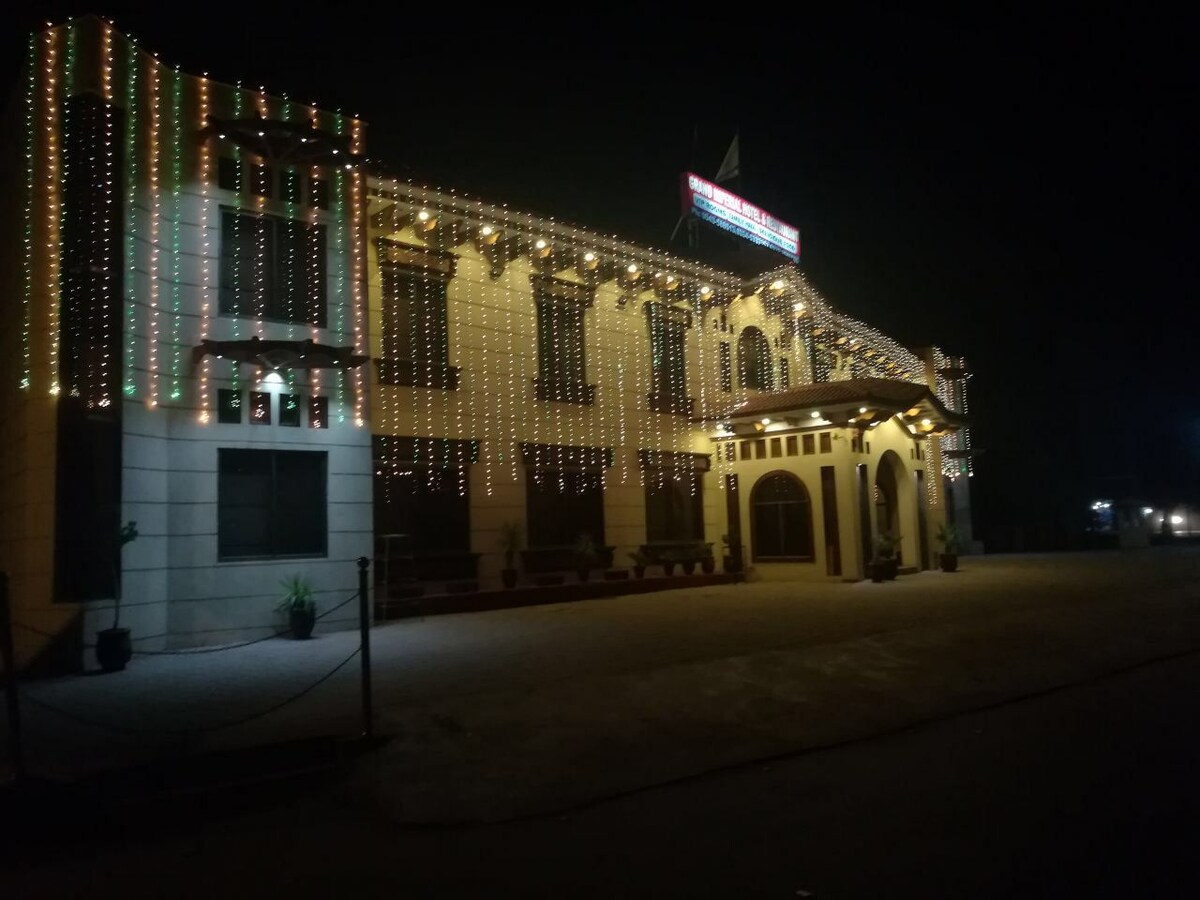 A building is adorned with decorative lights, illuminating its facade against the night sky. The entrance features an archway, and plants are placed along the pathway, enhancing the inviting appearance of the structure.