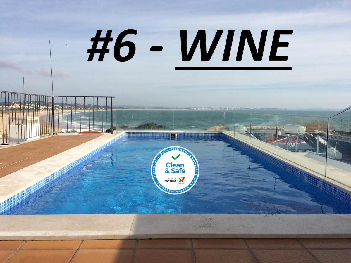 An outdoor swimming pool is visible on a terrace, featuring clear blue water and surrounded by a tiled deck. The ocean can be seen in the background along with a panoramic view of the city, offering a serene atmosphere for relaxation.