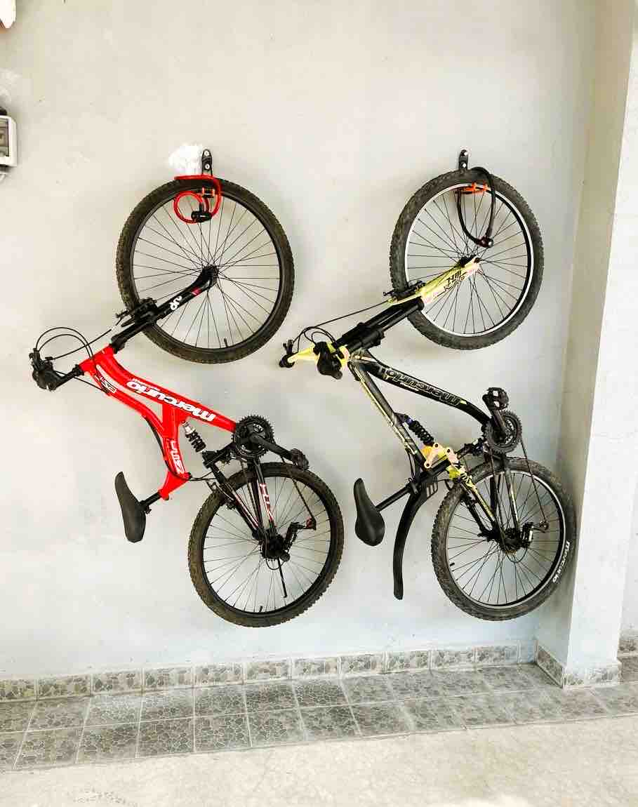 Two bicycles are mounted on a light-colored wall, with one bicycle featuring a red frame and the other in black with yellow accents. The floor below is tiled in a neutral gray tone, providing a tidy and functional storage solution.