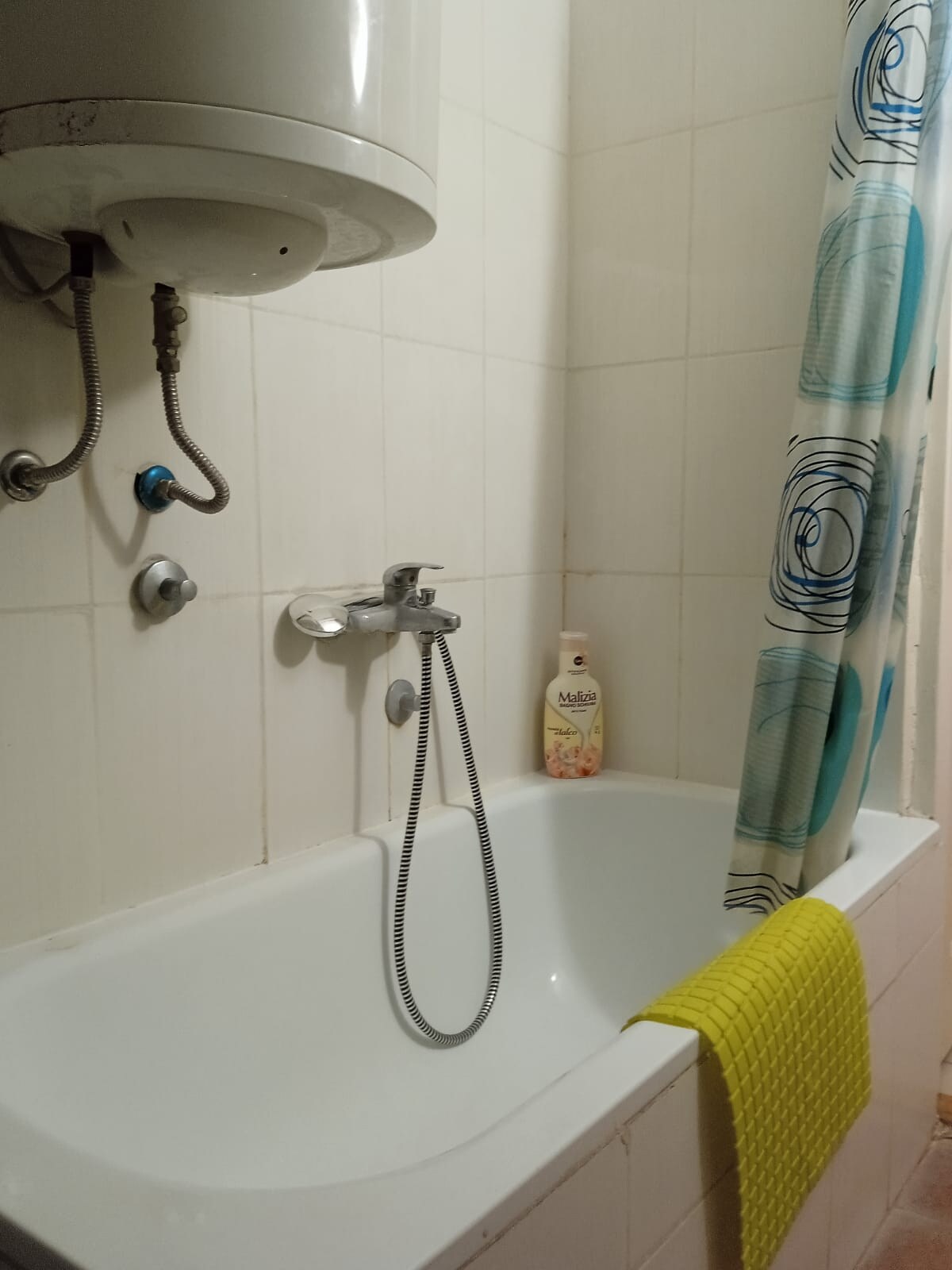 A clean bathroom is featured with a bathtub and a shower attachment. A green bath mat is positioned at the tub's edge, complementing the blue and white shower curtain. A soap dispenser is placed on the tub's rim, enhancing the functional space.