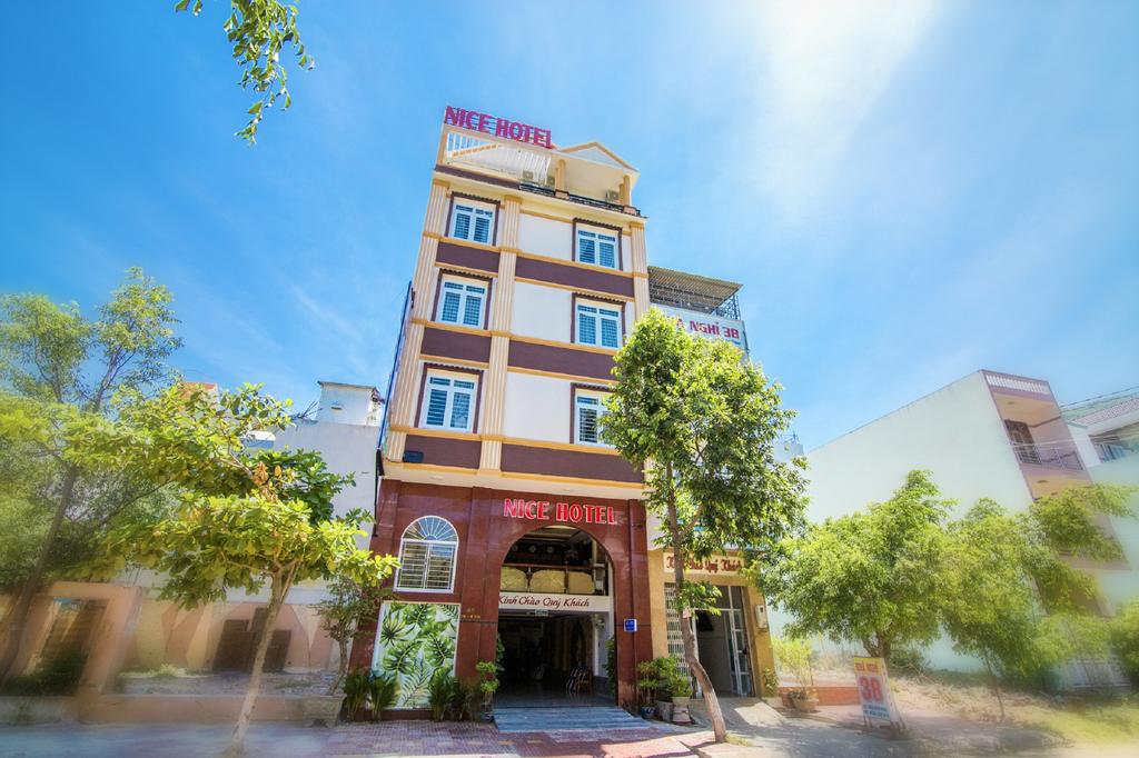 The exterior of the Nice Hotel is presented, showcasing a modern three-story building with a welcoming entrance. Lush trees and greenery surround the hotel, contributing to a pleasant atmosphere. A clear blue sky complements the overall ambiance.