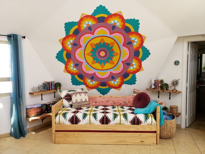 Colorful guest area with a twin daybed and trundle, accented by a vibrant mandala mural and cozy decor—perfect for kids, friends, or extra guests