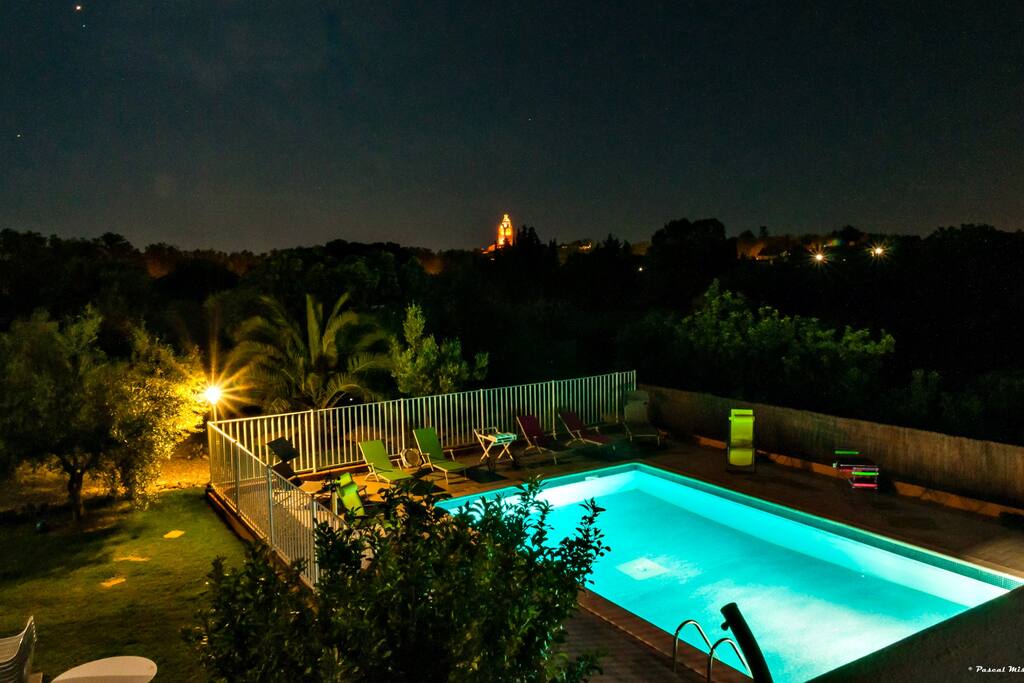 Vue via la terrasse des appartements sur la piscine et le clocher du village en soirée