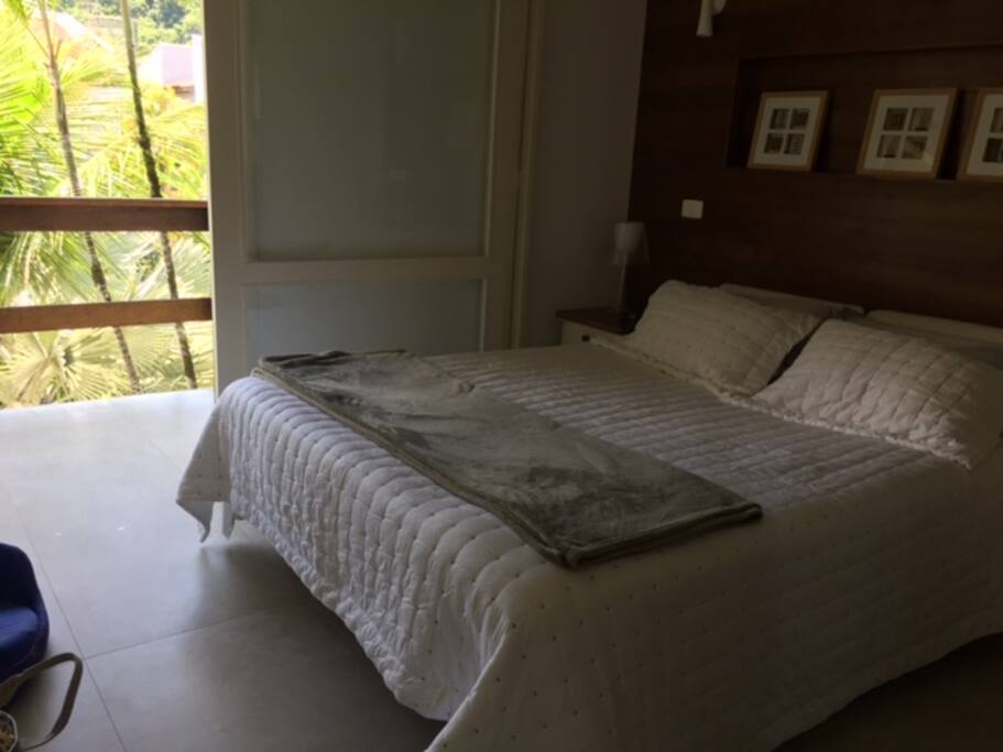 Suíte de casal 01 com varanda e vista para piscina do condomínio. Quarto com TV a cabo, ar-condicionado e ventilador